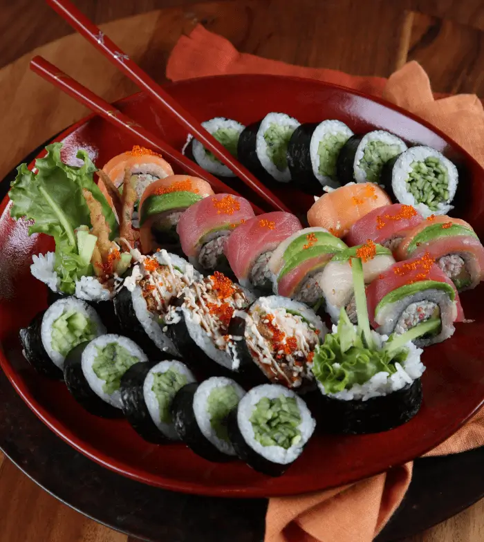 An image of a variety of sushi on a plate with a pair of red chopsticks.