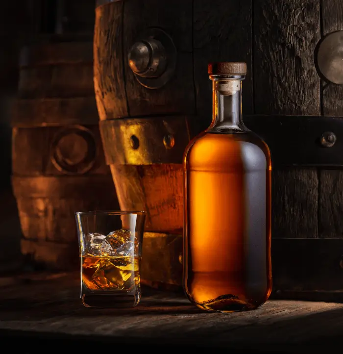 Two wooden barrel kegs, a bottle of alcohol and a glass with ice and alcohol in it.