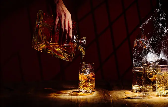 An image of a liquor being poured into a glass next to several glasses splashing.