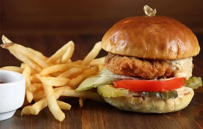 An image of chicken burger with lettuce, tomato and pickle and side of fries.