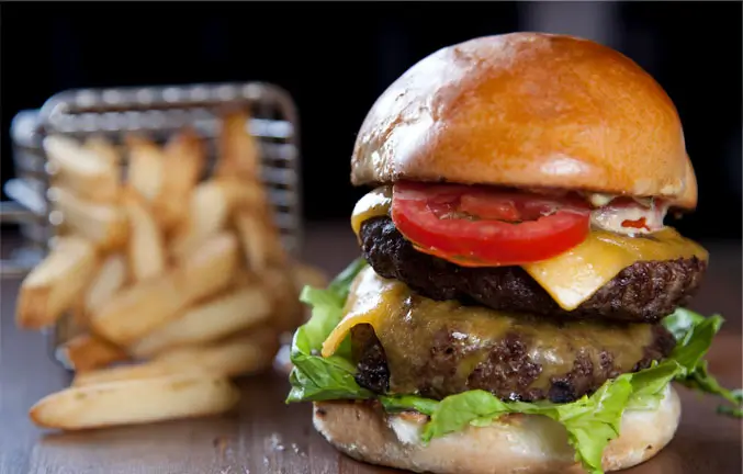 An image of a double cheeseburger with lettuce and tomatoes and a basket of fries.